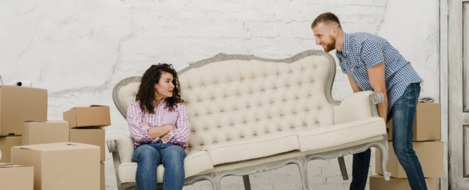 Man moving sofa with sitting woman
