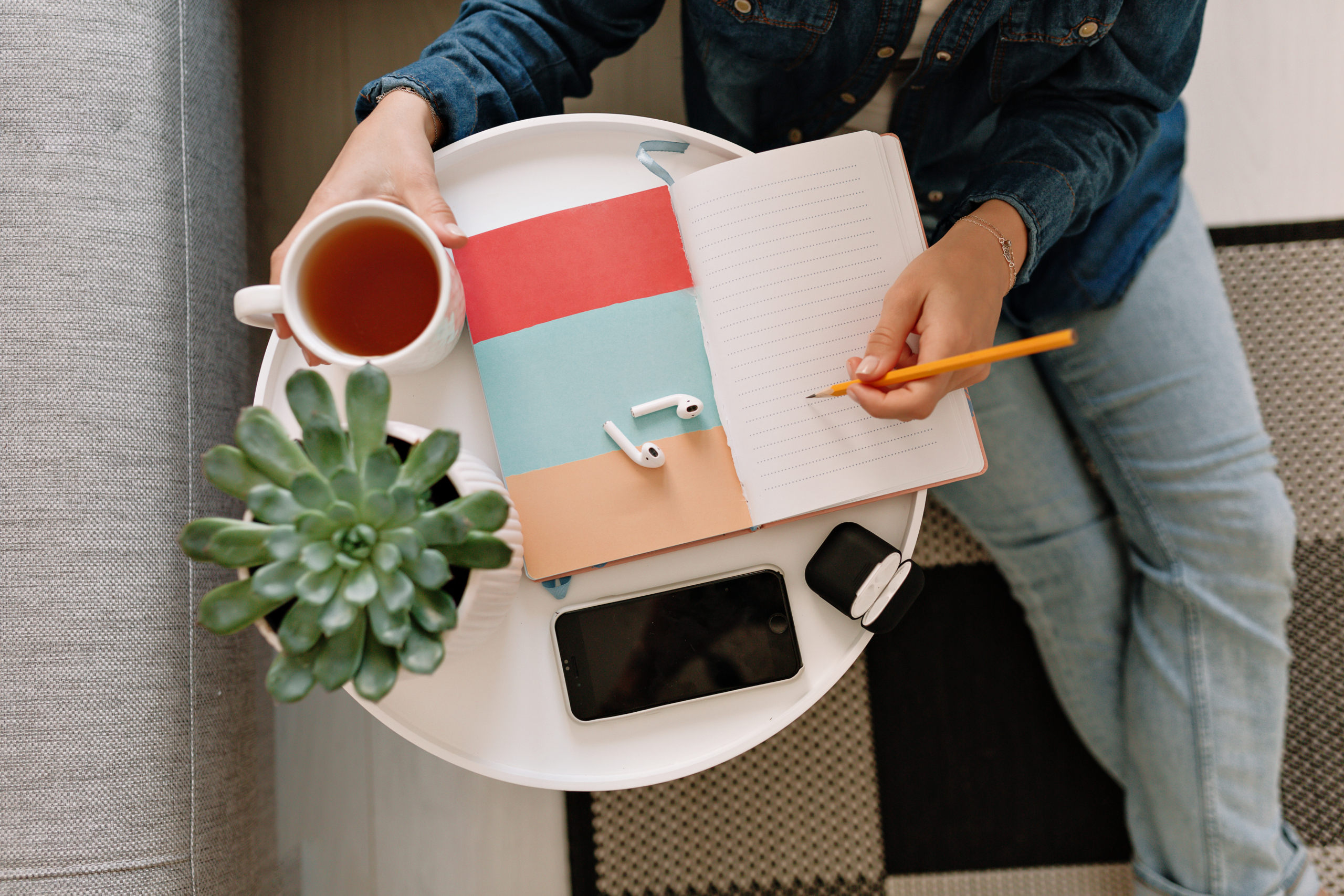 flat-lay-working-table-with-young-womans-hand-writing-notebook-with-smartphone-cup-tea-green-plant